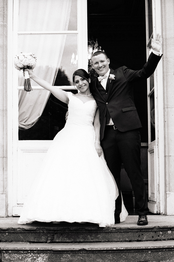 Photographie argentique du couple marié tout sourire devant le château de La Motte Fénelon 