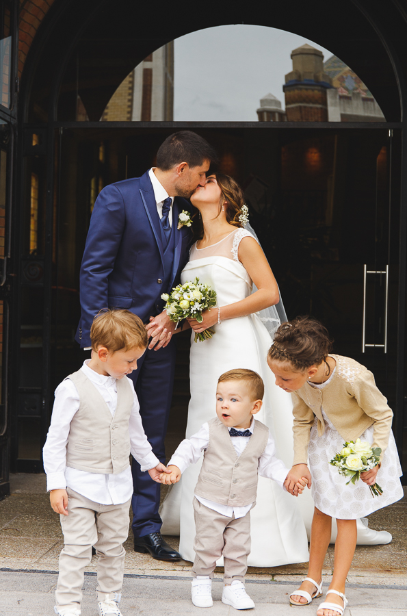 bisou couple fraîchement marié avec enfants d'honneur devant mairie de Comines photographe mariage famille Nord Lille Douai Arras