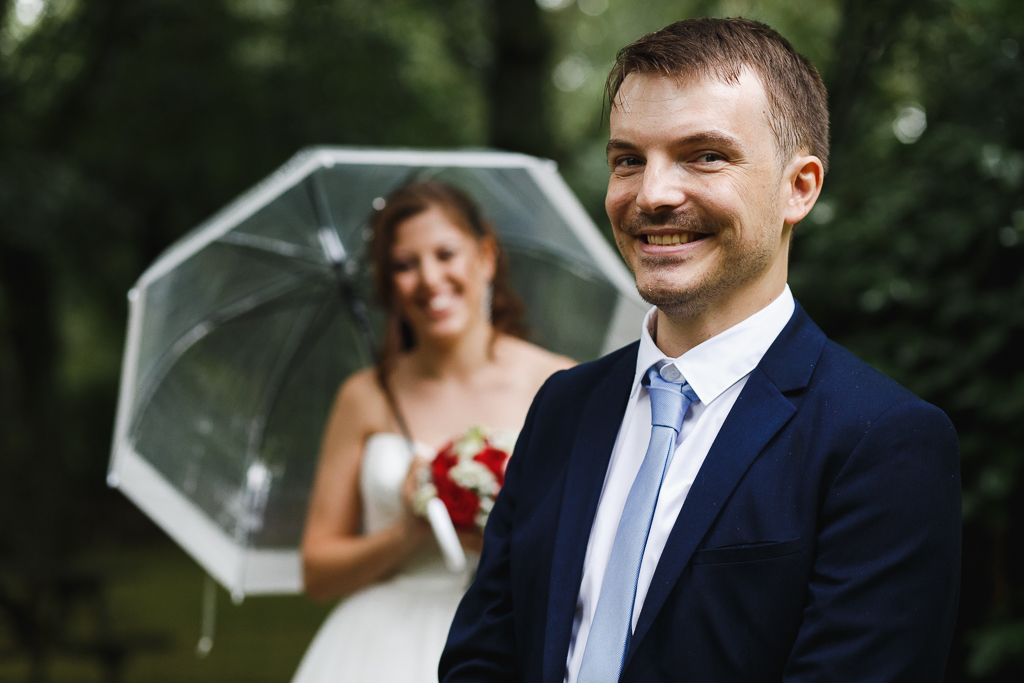 séance couple mariage Marcq en Barœul portrait du jeune marié avec mariée sous parapluie transparent en arrière-plan