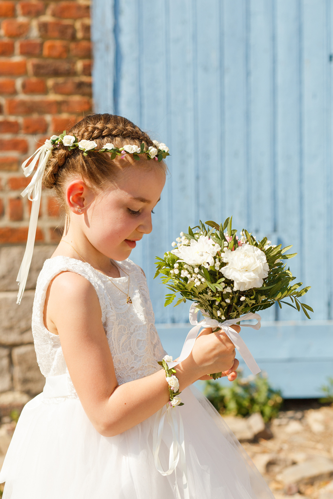 portrait demoiselle d'honneur dans robe de cérémonie blanche bracelet de fleur, petits bouquets coiffure tressée couronne de fleurs blanches ruban photographe mariage Nord