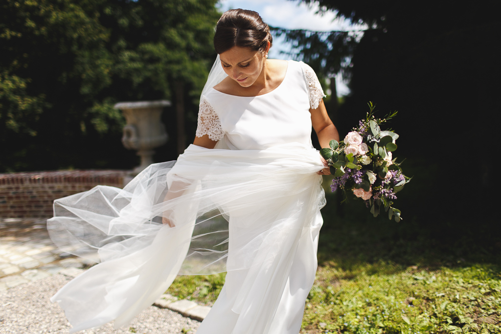 Détails de la robe Olivier Sinic reportage photo mariage à Morbecque. Bouquet et voile dans le vent. Mariage élégant au château de Morbecque. Photographie sur le vif mariage.