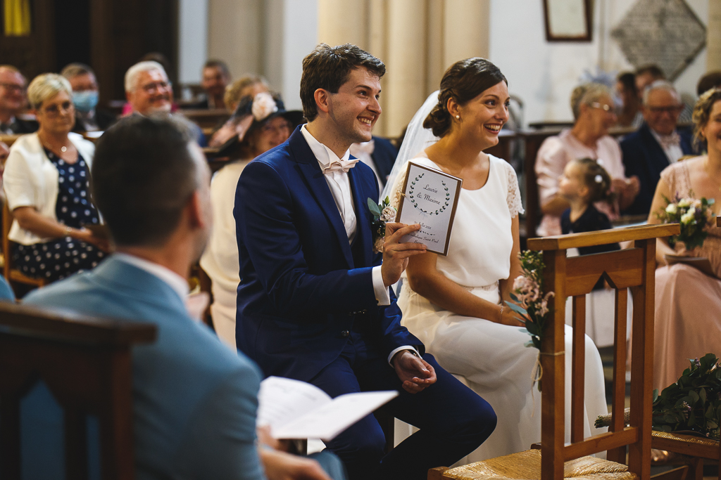 Le marié brandit le livret de cérémonie. Amusement de la mariée et des familles à l'église.