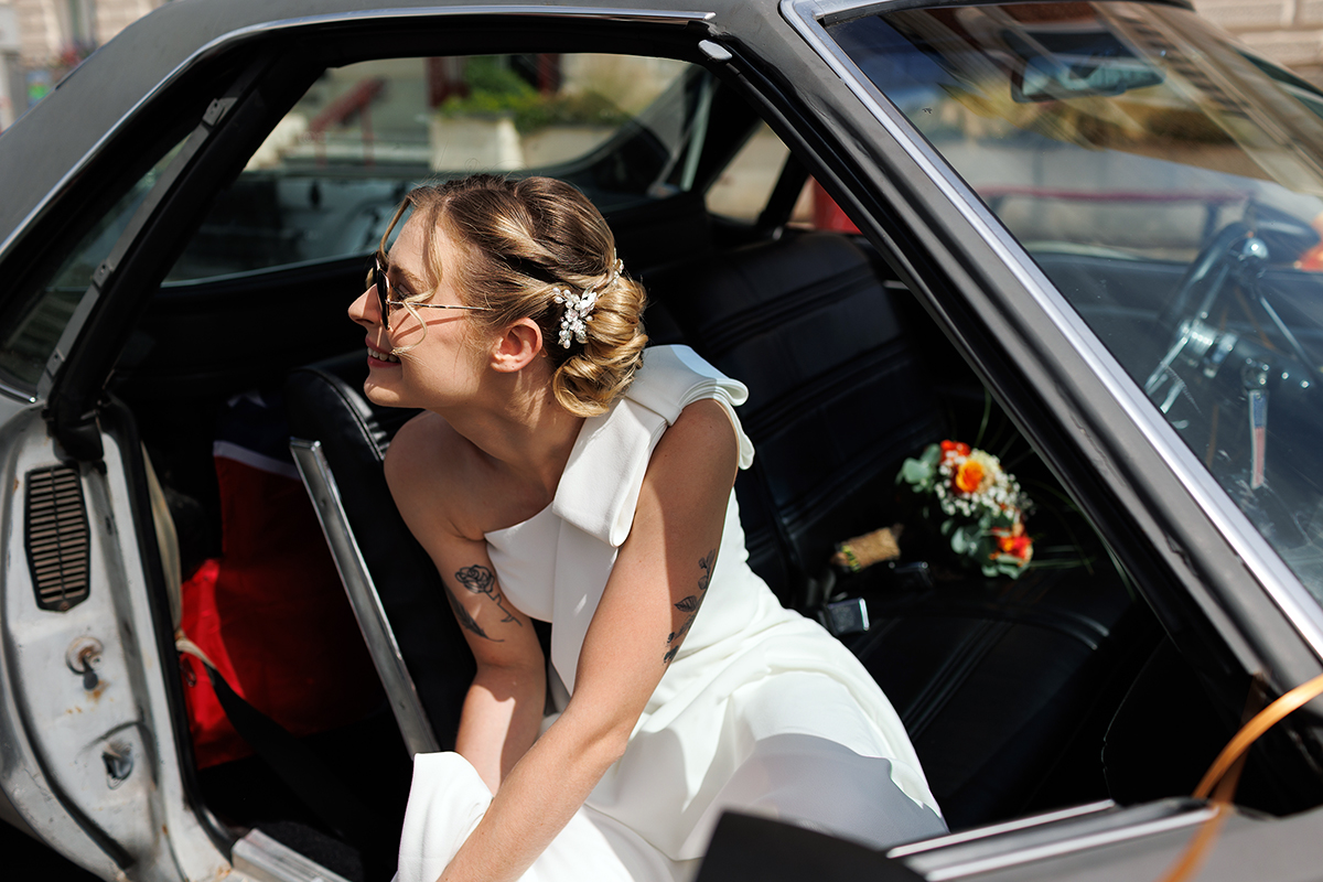 La mariée lunettes noires, tatouages et voiture de collection américaine. Photo vivante reportage mariage.