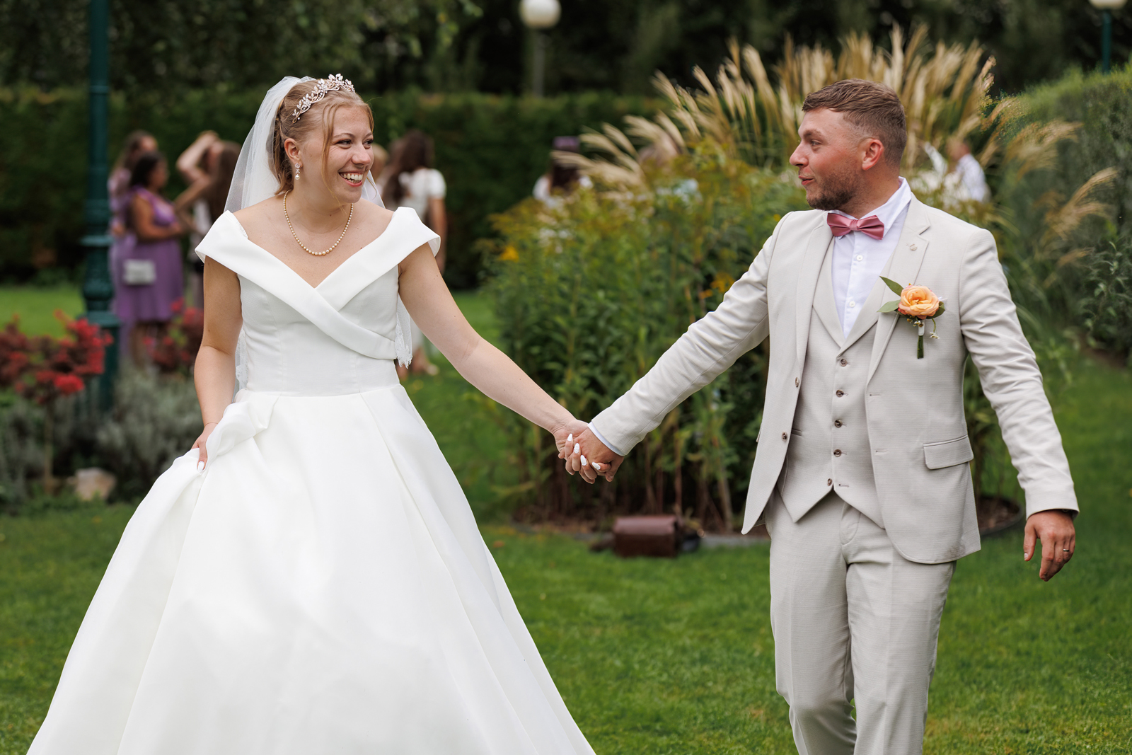couple main dans la main marchant dans le jardin du vin d'honneur.